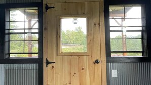 Eine Holztür mit Fenster, nebenan jeweils ein Fenster mit Metallrahmen.