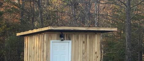 A small wooden shed with a white door and a number '5' on it, surrounded by trees.