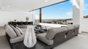 A modern living room with a large sofa, a dining area with a table and chairs, and a view of the cityscape through large windows.