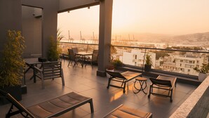 A balcony with a table and chairs, potted plants, and a view of a cityscape during sunset. - Unit for Living (Beirut)