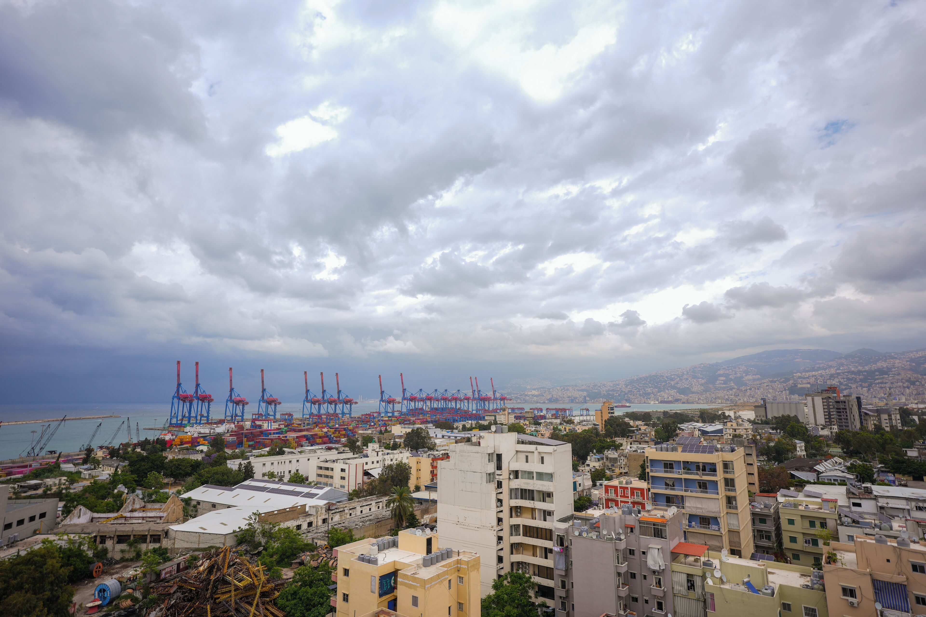 A coastal cityscape with industrial cranes, residential buildings, and a view of the sea.