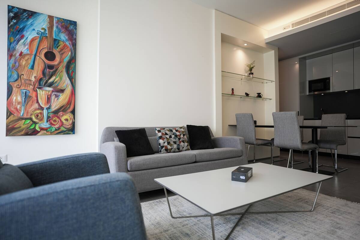A modern living room with a grey sofa, a coffee table, and a vibrant abstract painting on the wall.
