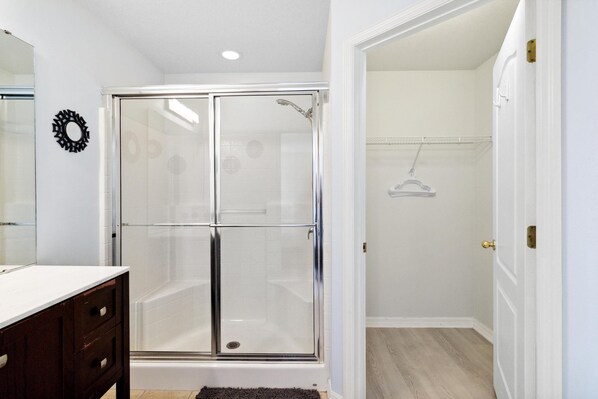 A modern bathroom with a glass shower enclosure, a white vanity with dark drawers, and a light-colored floor. - Great Community, amazing private pool, near Disney! (Davenport)