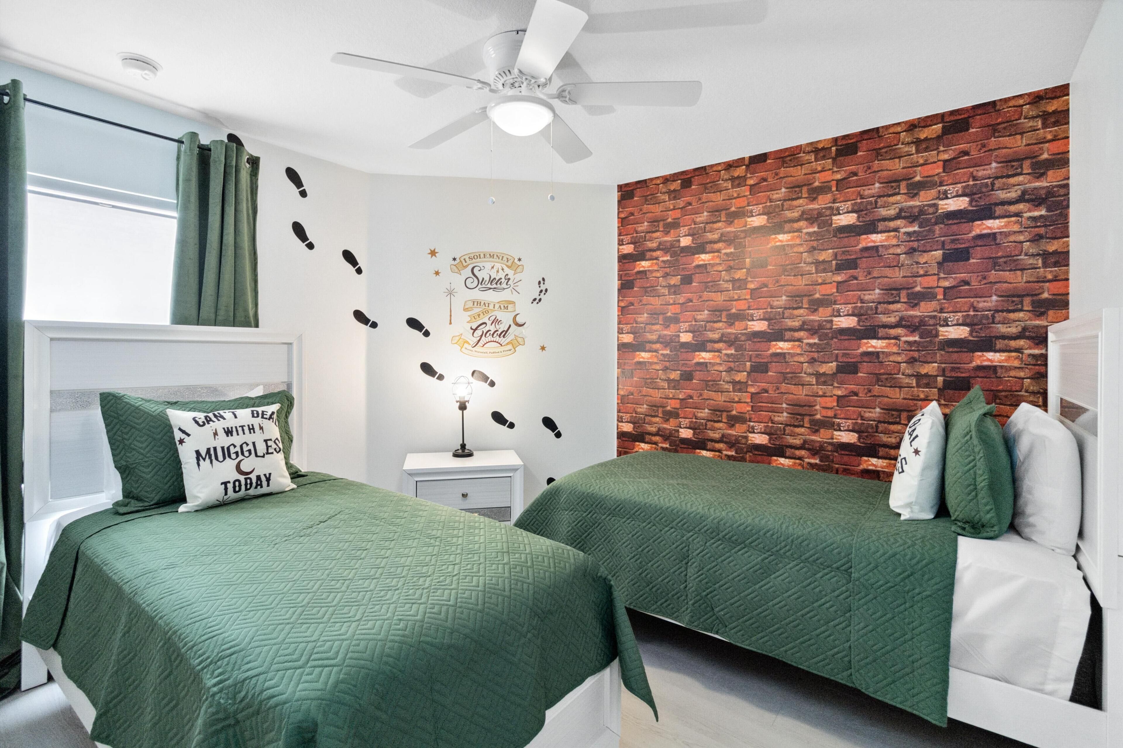 A bedroom with two beds, a brick wall, a ceiling fan, and a window with curtains.
