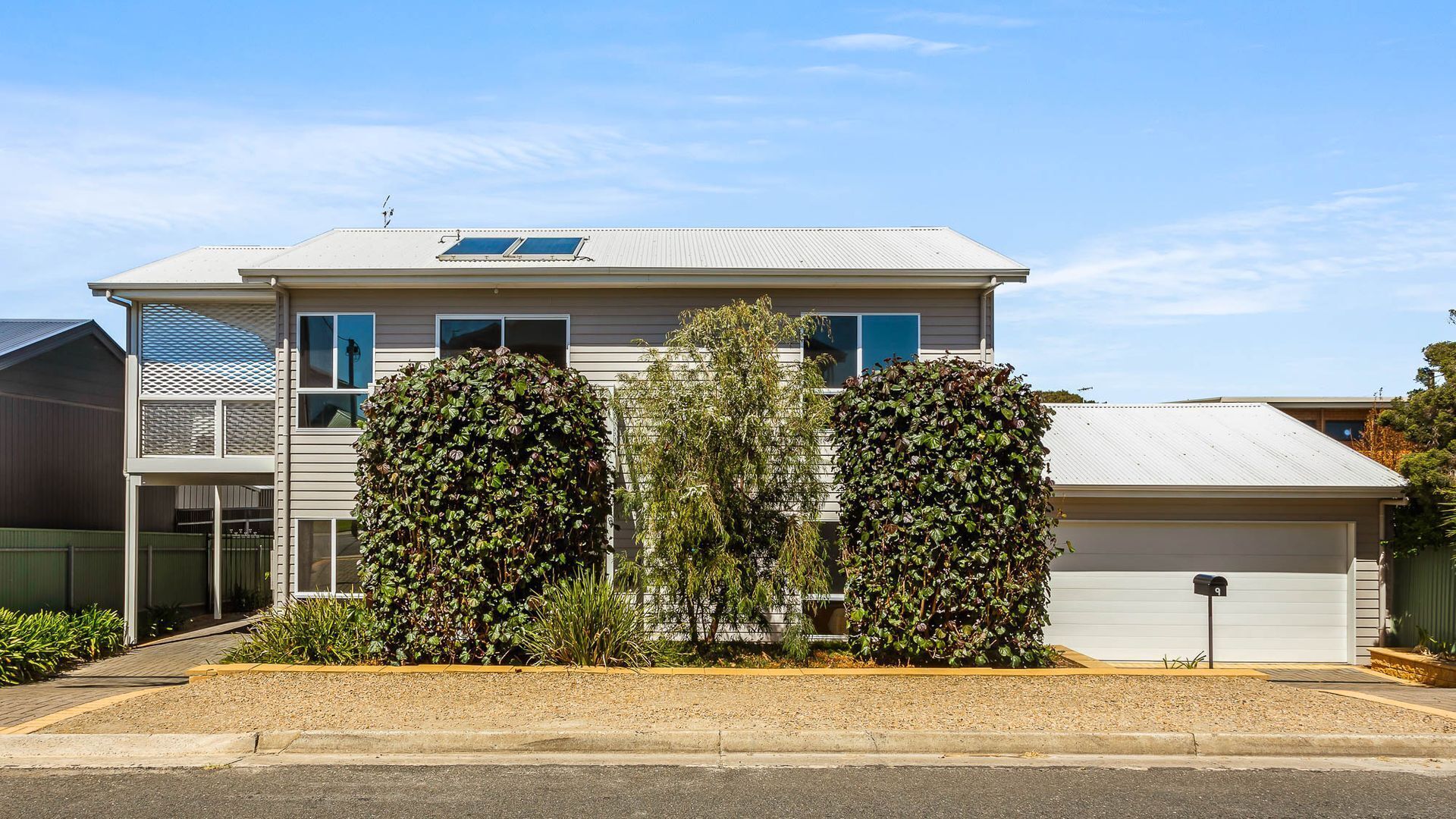 Een tweelaags huis met een garage, zonnepanelen en een goed onderhouden voortuin met twee grote struiken.