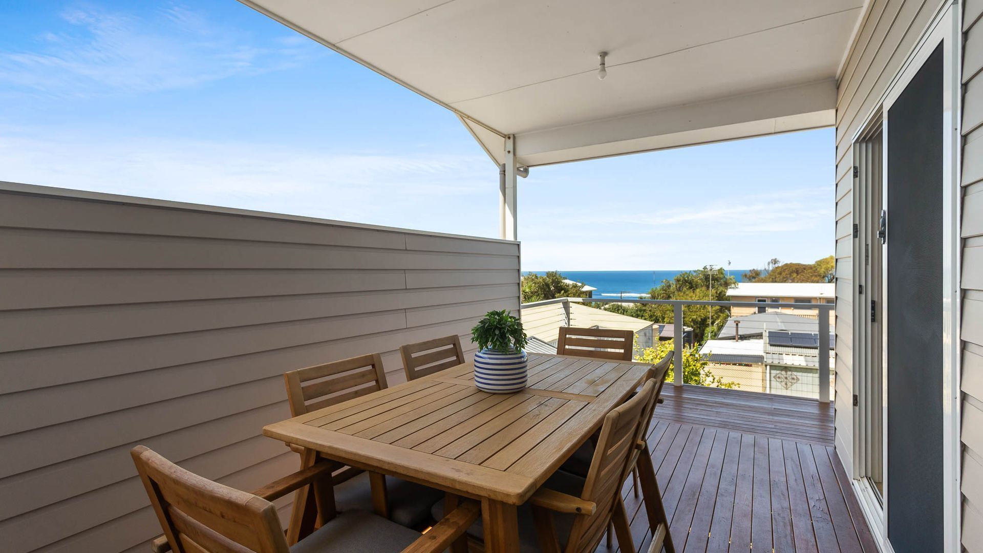 A wooden deck with a table and chairs, overlooking a coastal view.