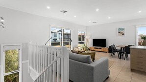 A modern living room with a grey sofa, a flat-screen TV, and a dining area with a wooden table and chairs.