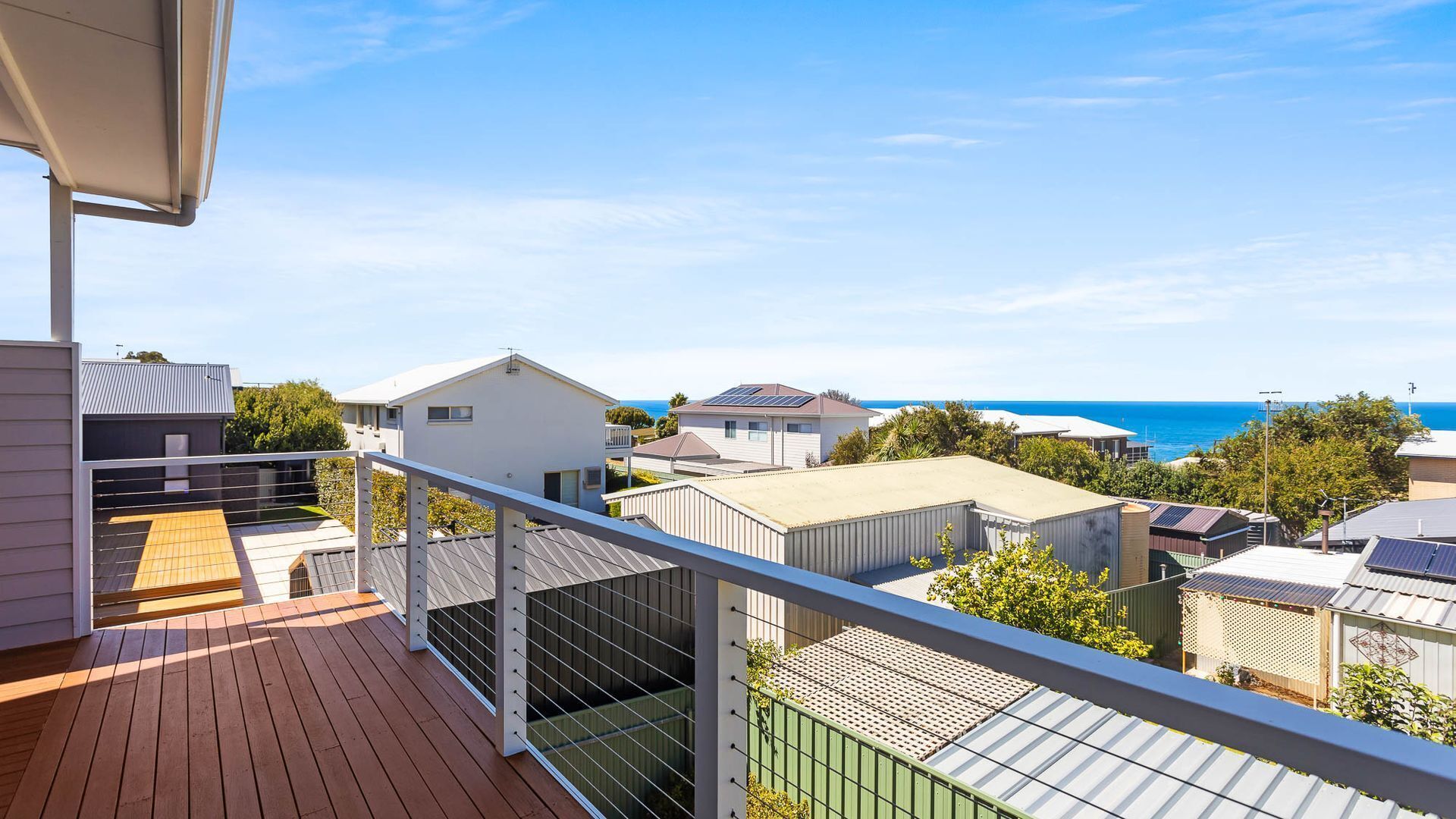 A balcony with a view of the sea, a wooden deck, and a metal railing.