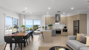 A modern kitchen with a central island, a dining area with a view, and a living area with a sofa.