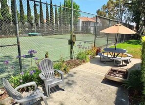 Un patio al aire libre con cancha de tenis, sillas y una mesa con sombrilla.