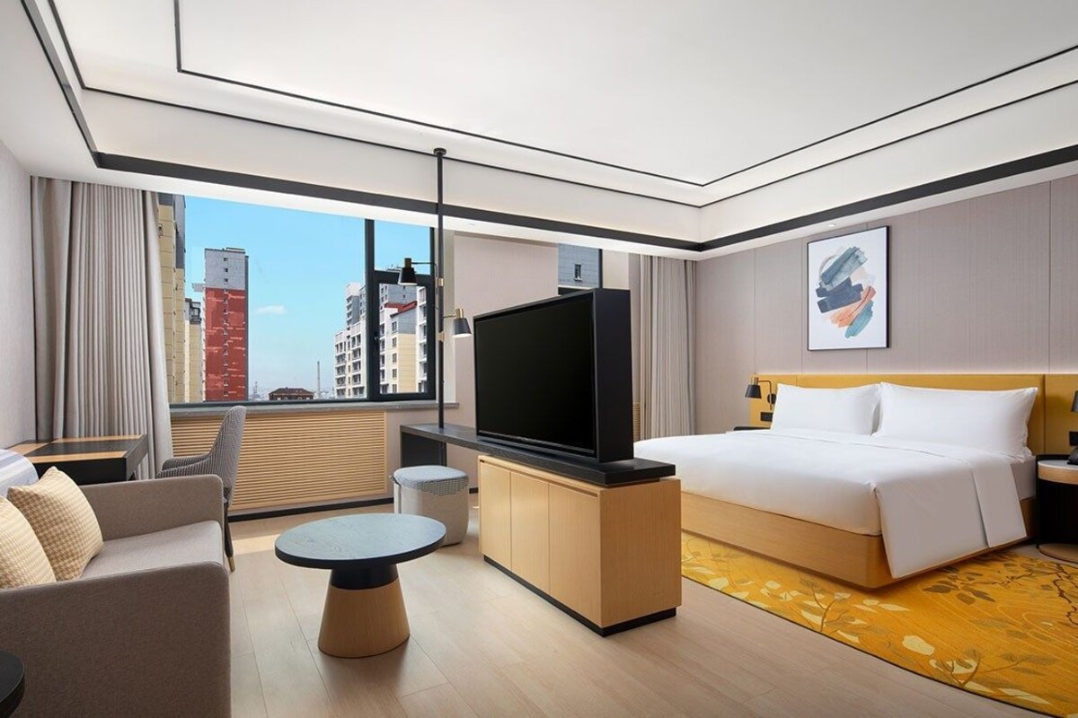 Une chambre d’hôtel moderne dotée d’un grand lit, d’un téléviseur à écran plat, d’un canapé, d’une petite table ronde et offrant une vue sur le paysage urbain.