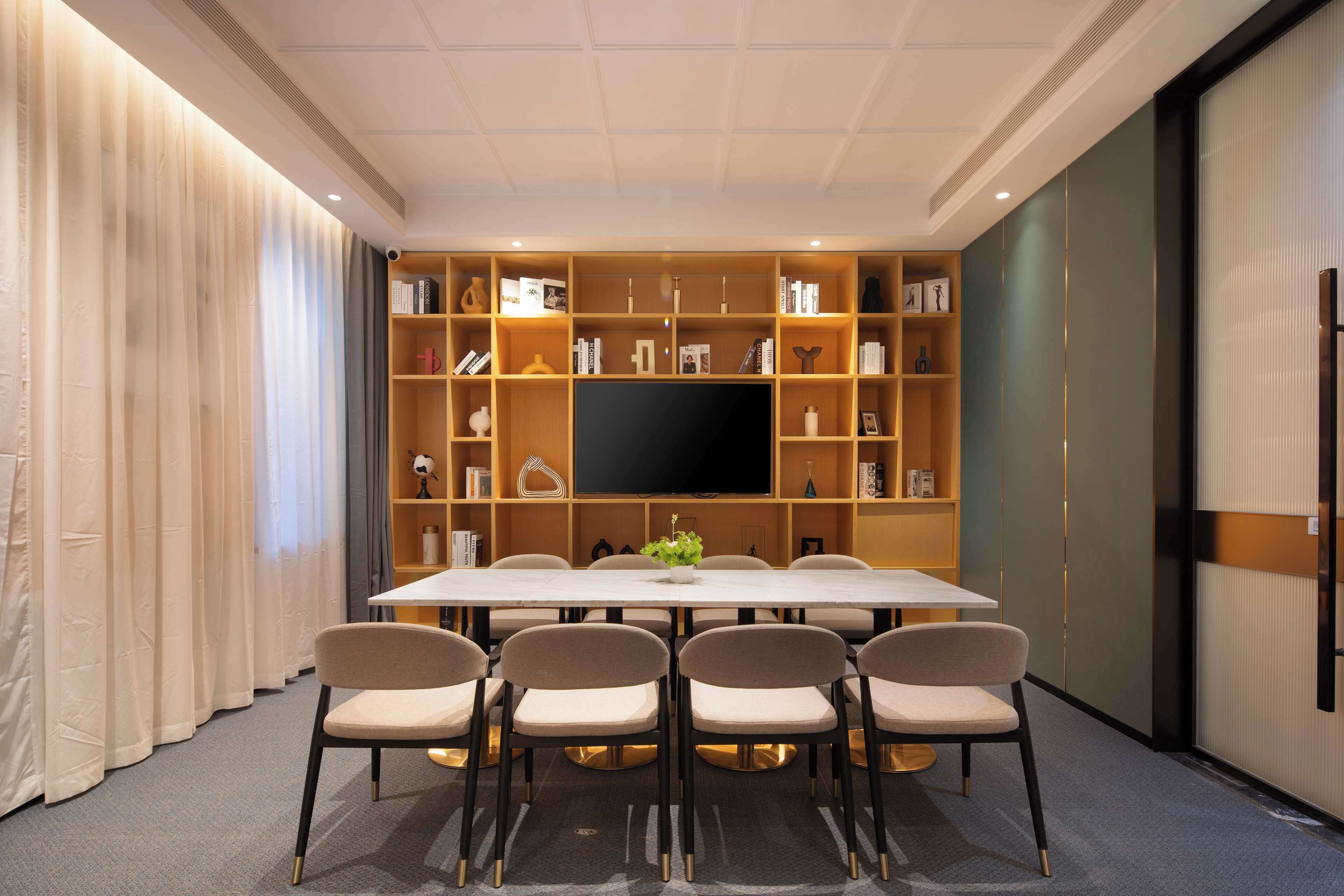 Una sala de conferencias con una larga mesa, seis sillas, un televisor de pantalla plana y una estantería llena de libros y objetos decorativos.