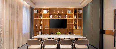 Una sala de conferencias con una larga mesa, seis sillas, un televisor de pantalla plana y una estantería llena de libros y objetos decorativos.