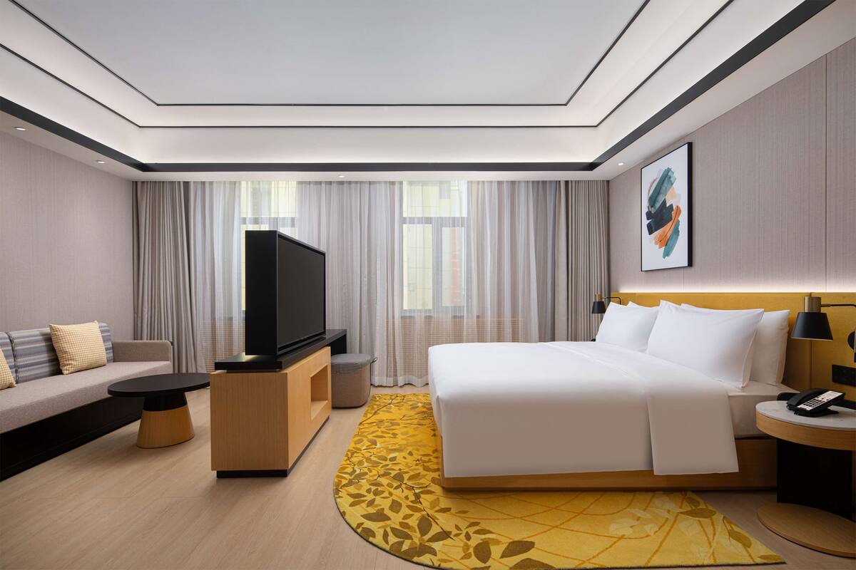 Ein modernes Hotelzimmer mit einer Couch, einem Bett, einem Fernseher, einem Nachttisch und einem kleinen Schreibtisch.