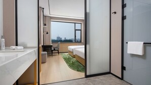 Moderni hotellihuone, jossa on sänky, työpöytä, tuoli, peilillä varustettu kylpyhuone ja näkymä kaupunkiin.