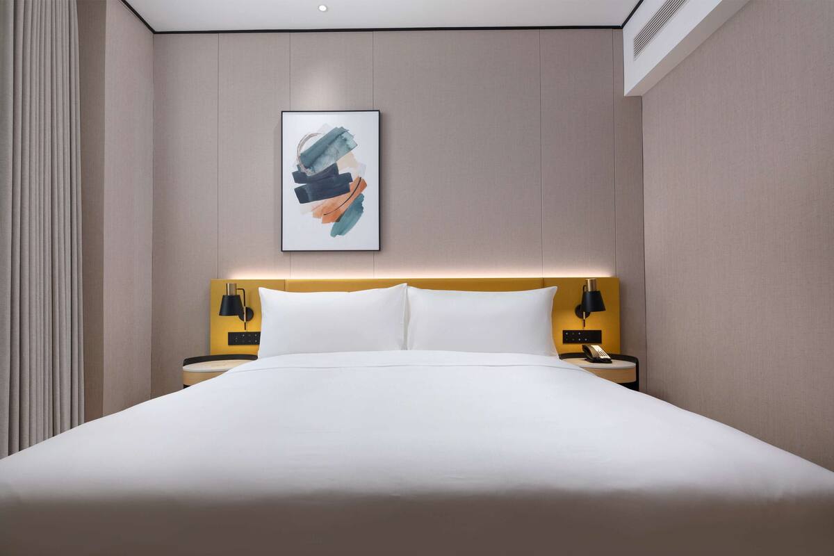 Ein Hotelzimmer mit einem großen Bett, zwei Nachttischen mit Lampen, einem Wandbild und einem Fenster mit Vorhängen.