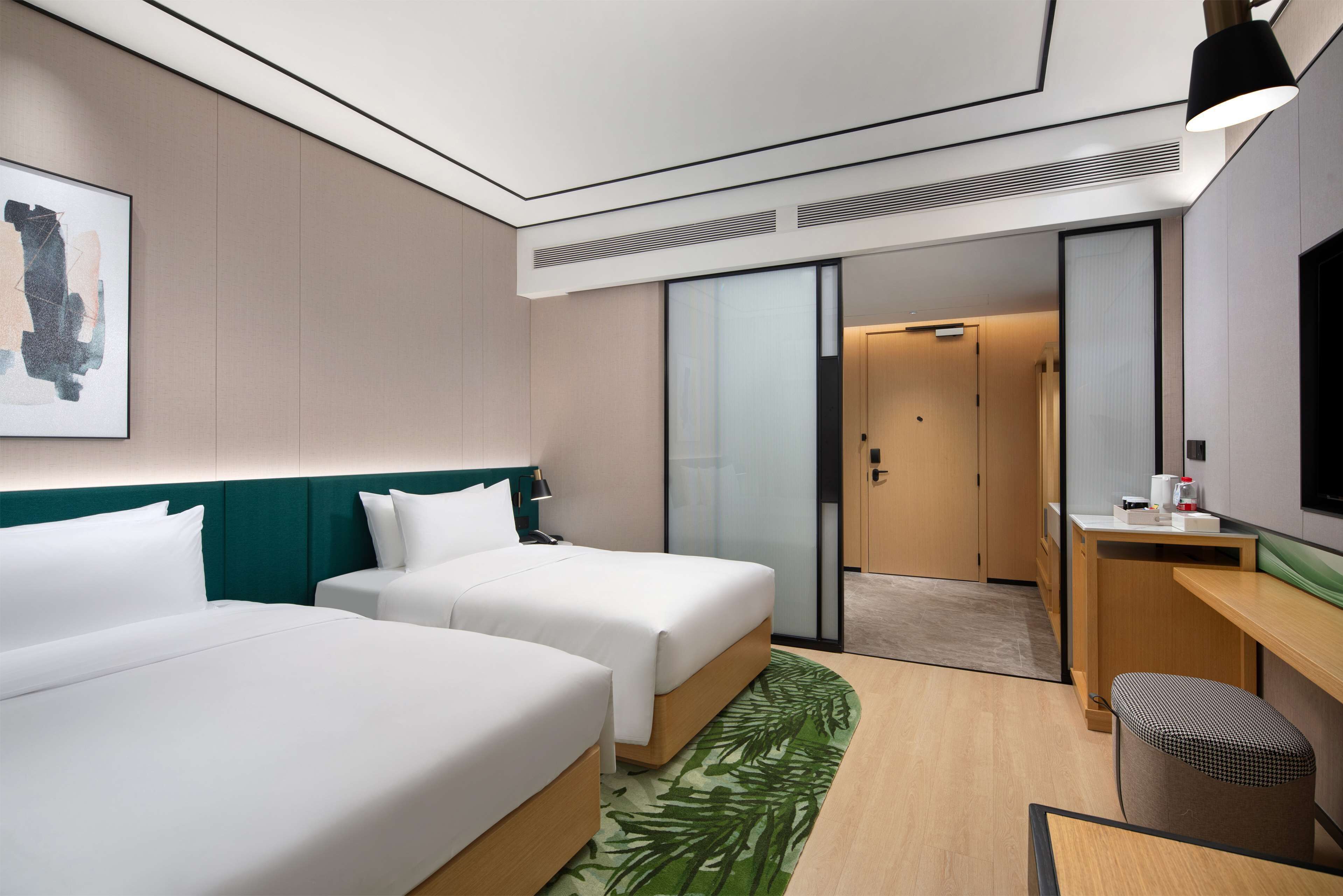 A hotel room with two beds, a desk, a chair, a television, and a painting on the wall.