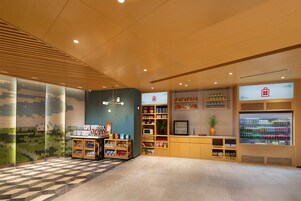 Un interior moderno con paneles de madera en el techo, una recepción, un refrigerador lleno de bebidas y una exhibición de aperitivos y libros.