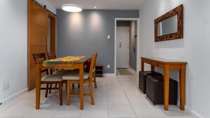 A dining area with a wooden table and chairs, a colorful tablecloth, a sliding door, a mirror on the wall, and a small table with a vase. - For Families 10min From Copacabana Beach Pl804 (Rio de Janeiro)