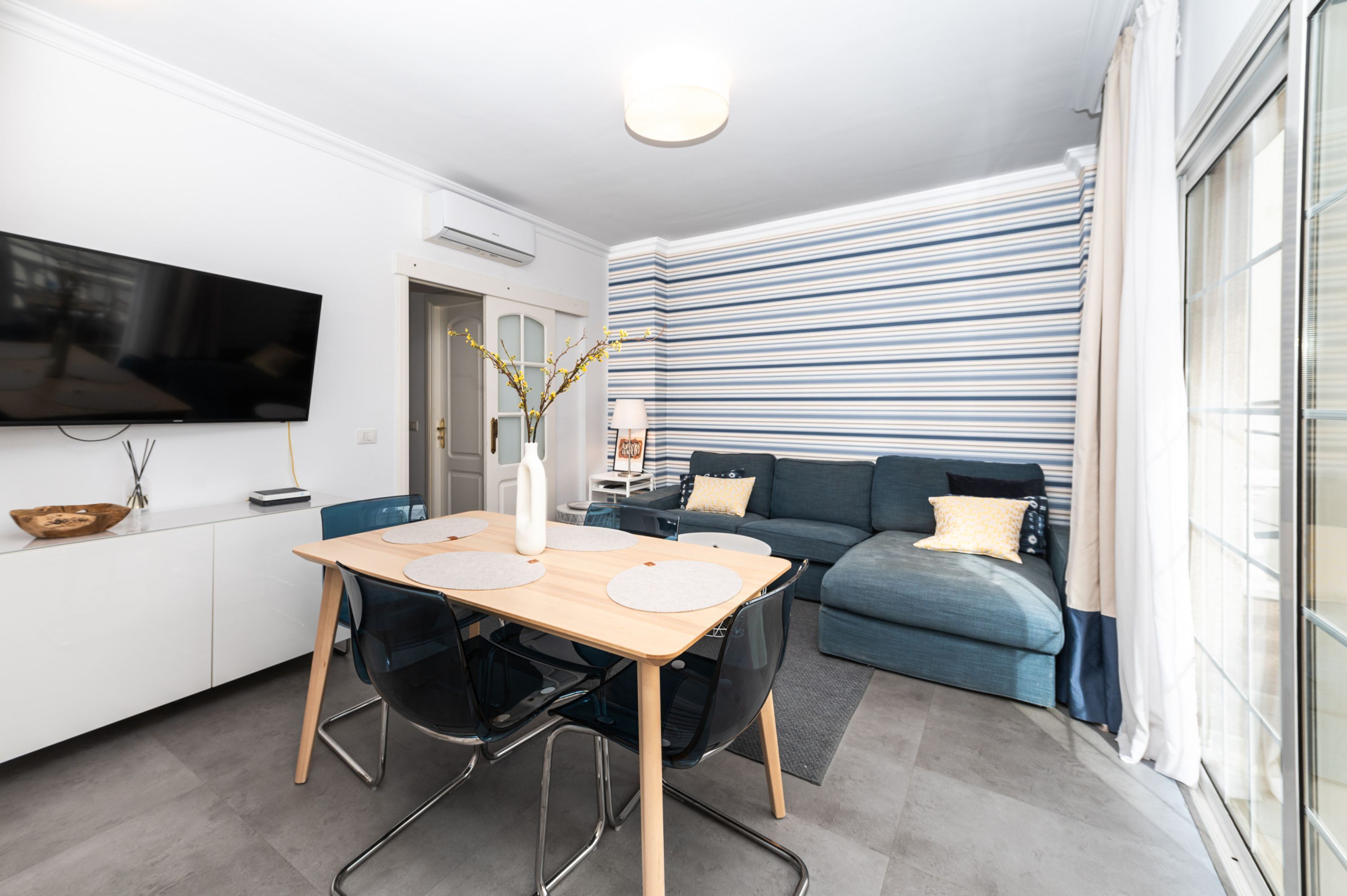 Una sala de estar moderna con comedor, un sofá y un televisor montado en la pared.