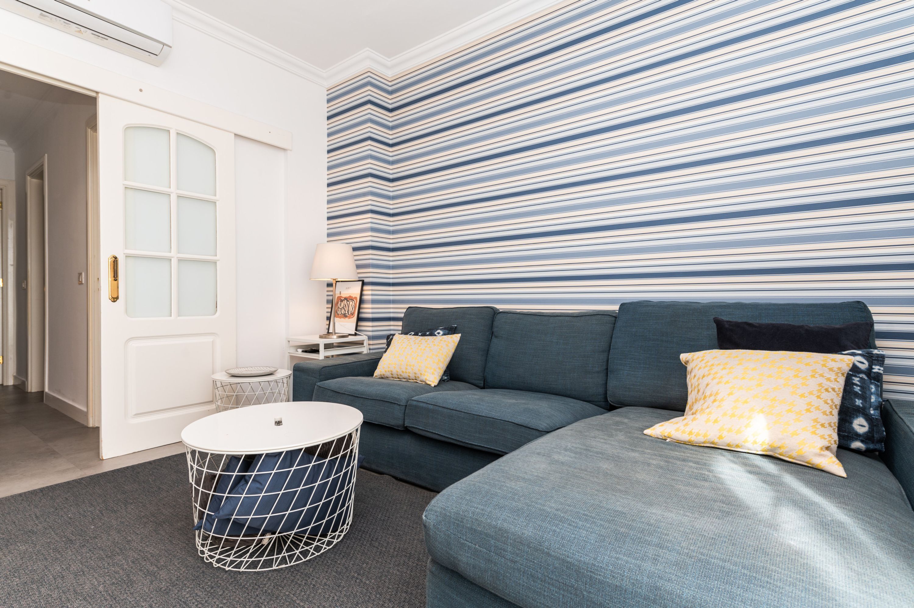 Ein modernes Wohnzimmer mit einer Eckcouch, einem runden Couchtisch und einer gestreiften Wand.
