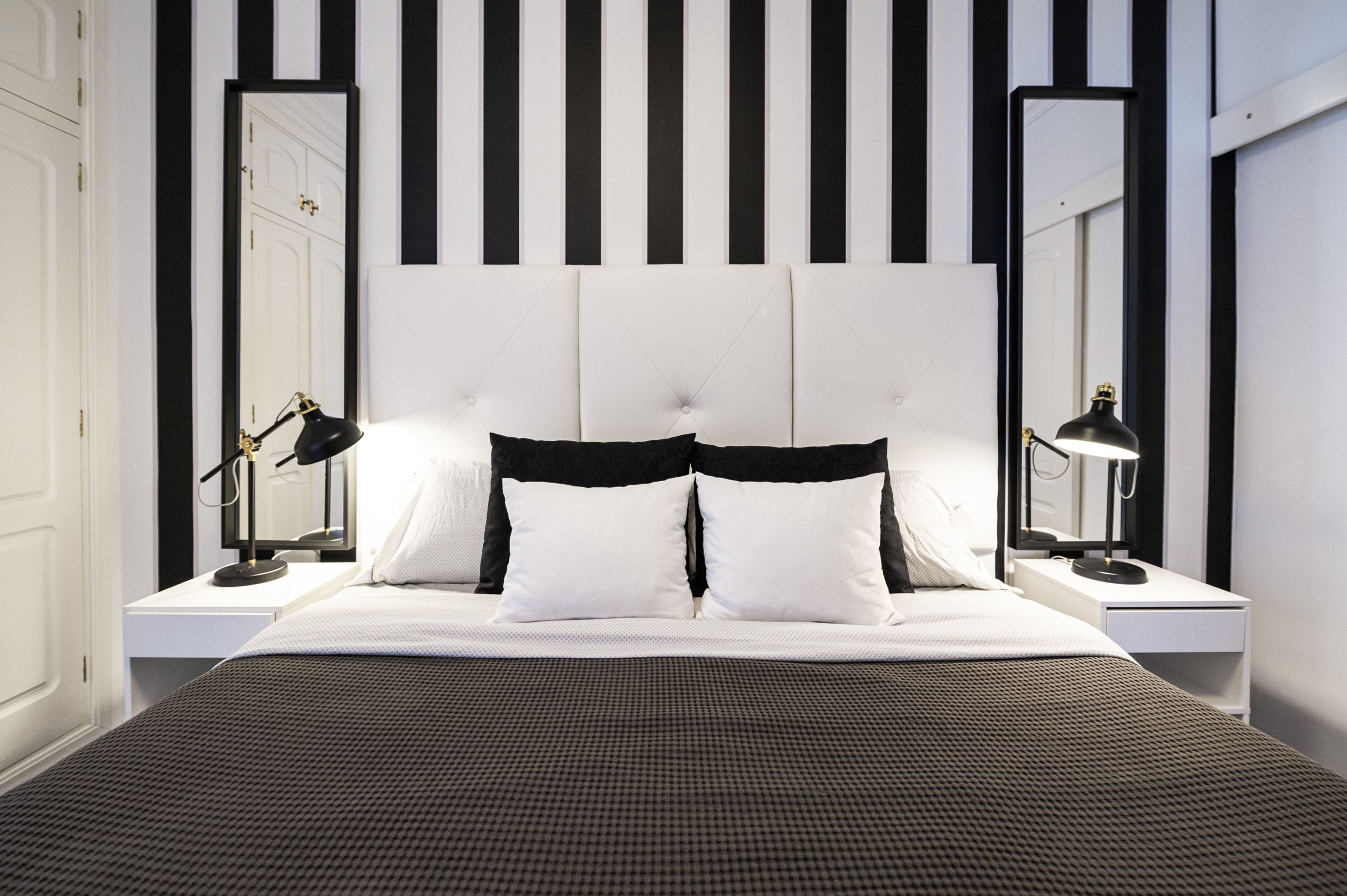 A modern bedroom with a large bed, two bedside tables, and a headboard with vertical stripes.