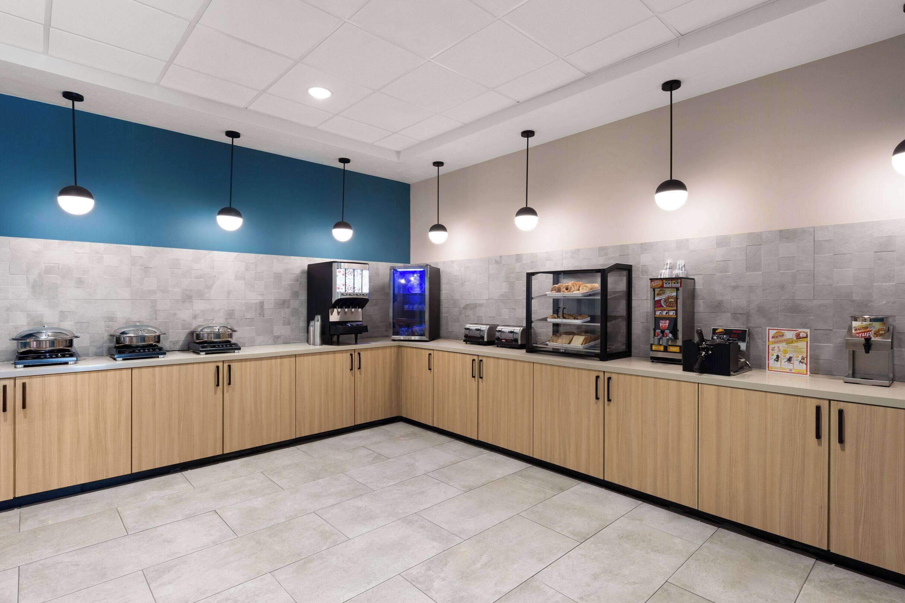 A modern kitchen with wooden cabinets, a blue accent wall, and various appliances like a coffee machine and a toaster.