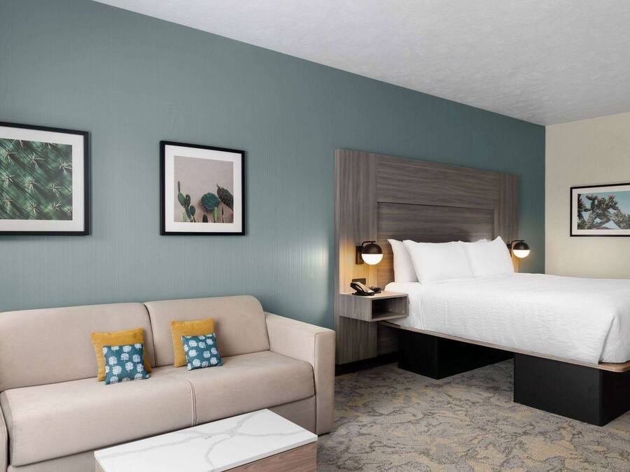 Quarto de hotel com uma cama, um sofá e duas imagens emolduradas na parede.