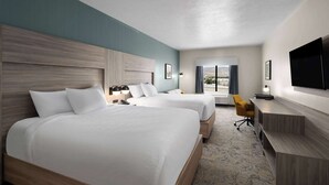 Quarto de hotel com duas camas, uma escrivaninha, uma televisão e vista para o exterior.