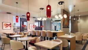 Uma sala de jantar moderna com mesas e cadeiras redondas, luminárias pendentes vermelhas e obras de arte nas paredes.