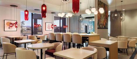 A modern dining area with round tables and chairs, red pendant lights, and artwork on the walls.