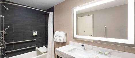A modern bathroom with a bathtub, a large mirror, and a vanity with a marble countertop.