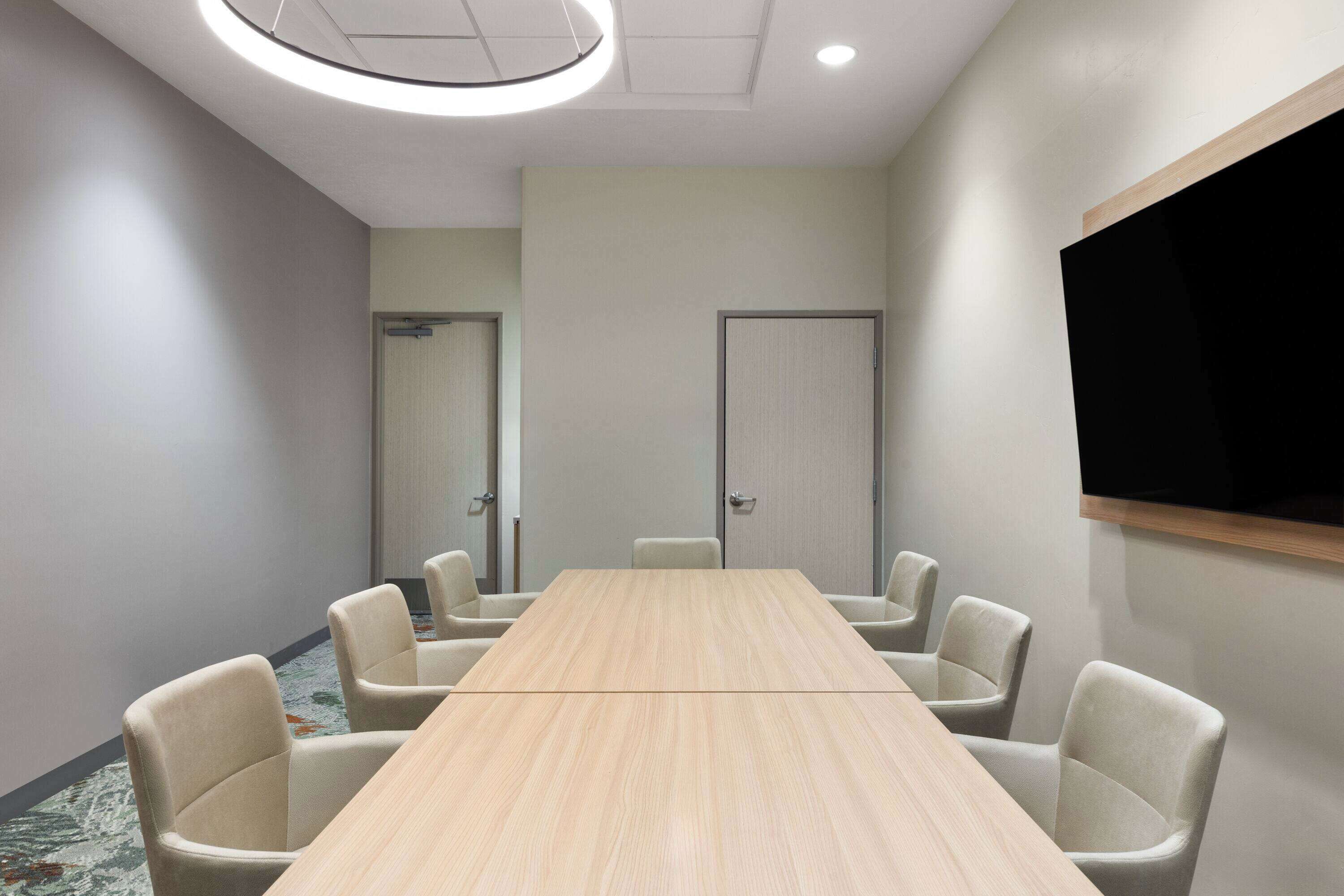 A conference room with a long table, six chairs, a flat-screen TV, and two doors.