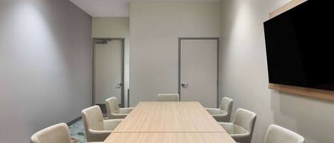 A conference room with a long table, six chairs, a flat-screen TV, and two doors.