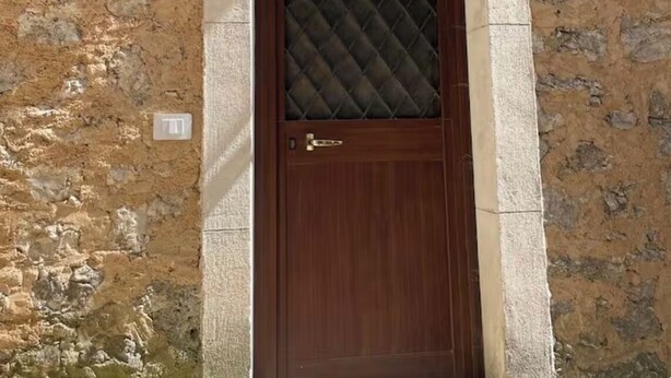 Ein Steinhaus mit einer Holztür, einem kleinen Fenster und einer Lampe über der Tür.