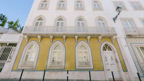 Un bâtiment à la façade blanche, doté de nombreuses fenêtres en arc de cercle et d’un balcon orné de balustrades décoratives.