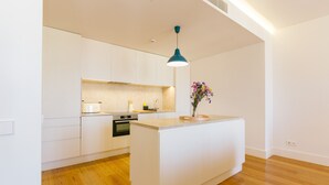 Une cuisine moderne avec des meubles blancs, un îlot central et un luminaire suspendu bleu.