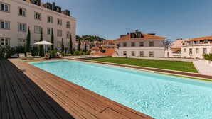 Une piscine dotée d’une terrasse en bois, entourée de bâtiments au style architectural classique.