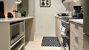 A modern kitchen with a built-in oven, a microwave, and a sink. There is a black and white rug on the floor, and a potted plant on the counter.
