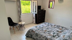 Een slaapkamer met een bed, een stoel, een dressoir, een raam met gordijnen en een kleine tafel.