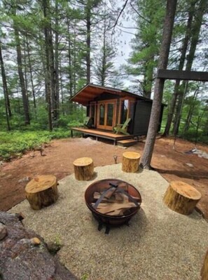 A cabin with a wooden deck and a fire pit surrounded by tree stump seating.