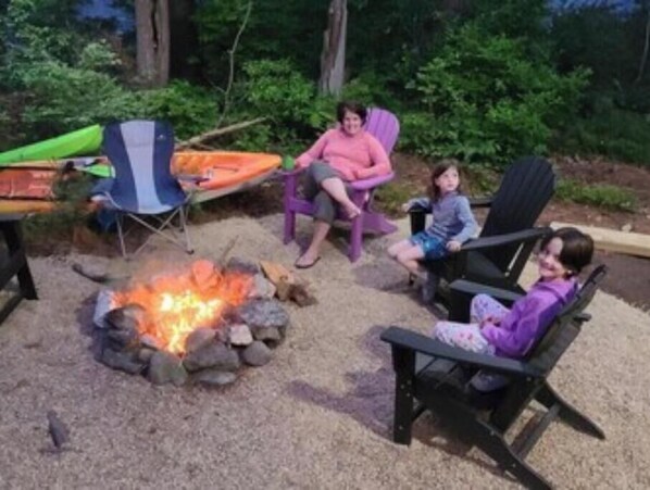 A campfire with rocks, a green tent, and two chairs.
