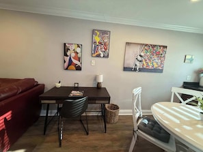 Un salon avec une table à manger en bois foncé, un canapé rouge, une chaise blanche et un lit blanc. Il y a trois tableaux accrochés au mur.