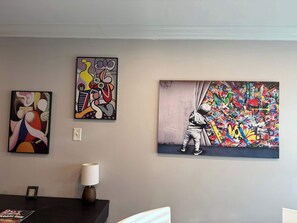 A dining area with a table, chairs, a lamp, and three artworks on the wall.