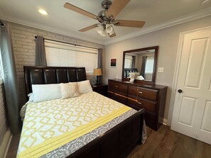 A bedroom with a bed, a dresser, a ceiling fan, a mirror, and a door.
