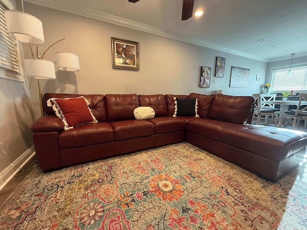 A brown leather sectional sofa with decorative pillows, a patterned rug, and wall art in a living room with a dining area in the background. - Parking | 5 min downtown | WD | TV bedroom | Pool (Baton Rouge)