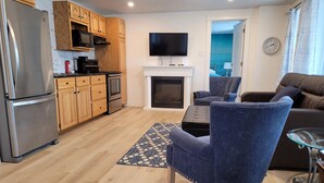 A modern kitchen with wooden cabinets, a stainless steel refrigerator, and a flat-screen TV mounted above the fireplace.