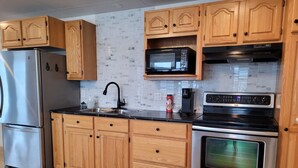 A modern kitchen with wooden cabinets, a stainless steel refrigerator, a microwave, a coffee maker, and an oven.