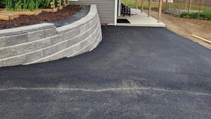 A residential driveway leading to a house with a covered porch and a garden area with raised beds.