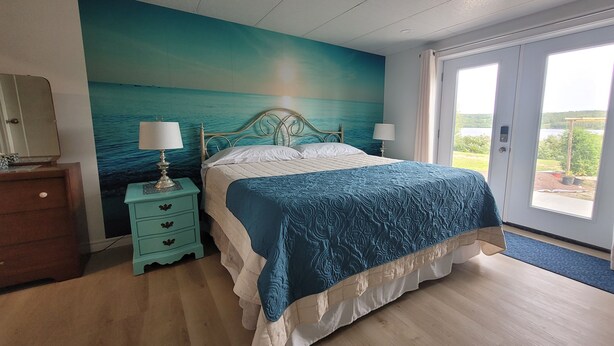 A bedroom with a bed, a nightstand, a dresser, a window, and a view of the outdoors.